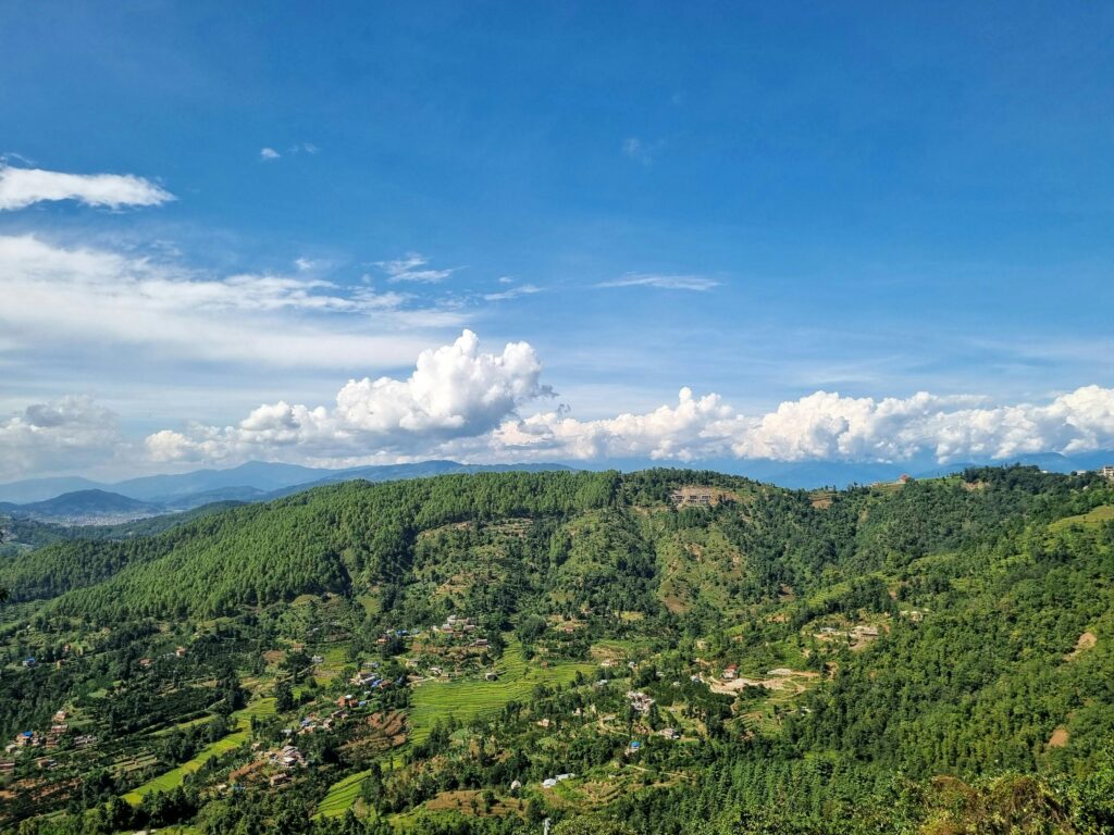 Peaceful landscape of lush green hills and village under blue sky in Nepal.